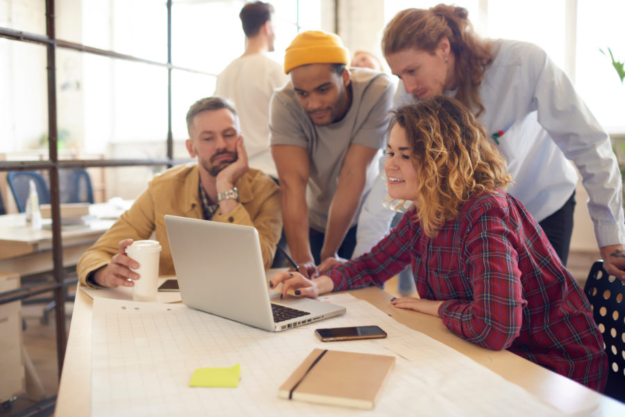 Diverse group of young adults looking over a laptop together with papers and notebooks